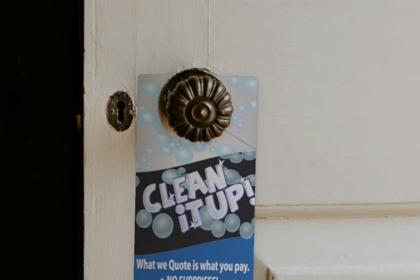 Clean It Up carpet cleaning door hanger hung on a brass doorknob through its die-cut hole, with a soap-bubble design, "No surprises, no hidden fees" and a 20% off coupon.