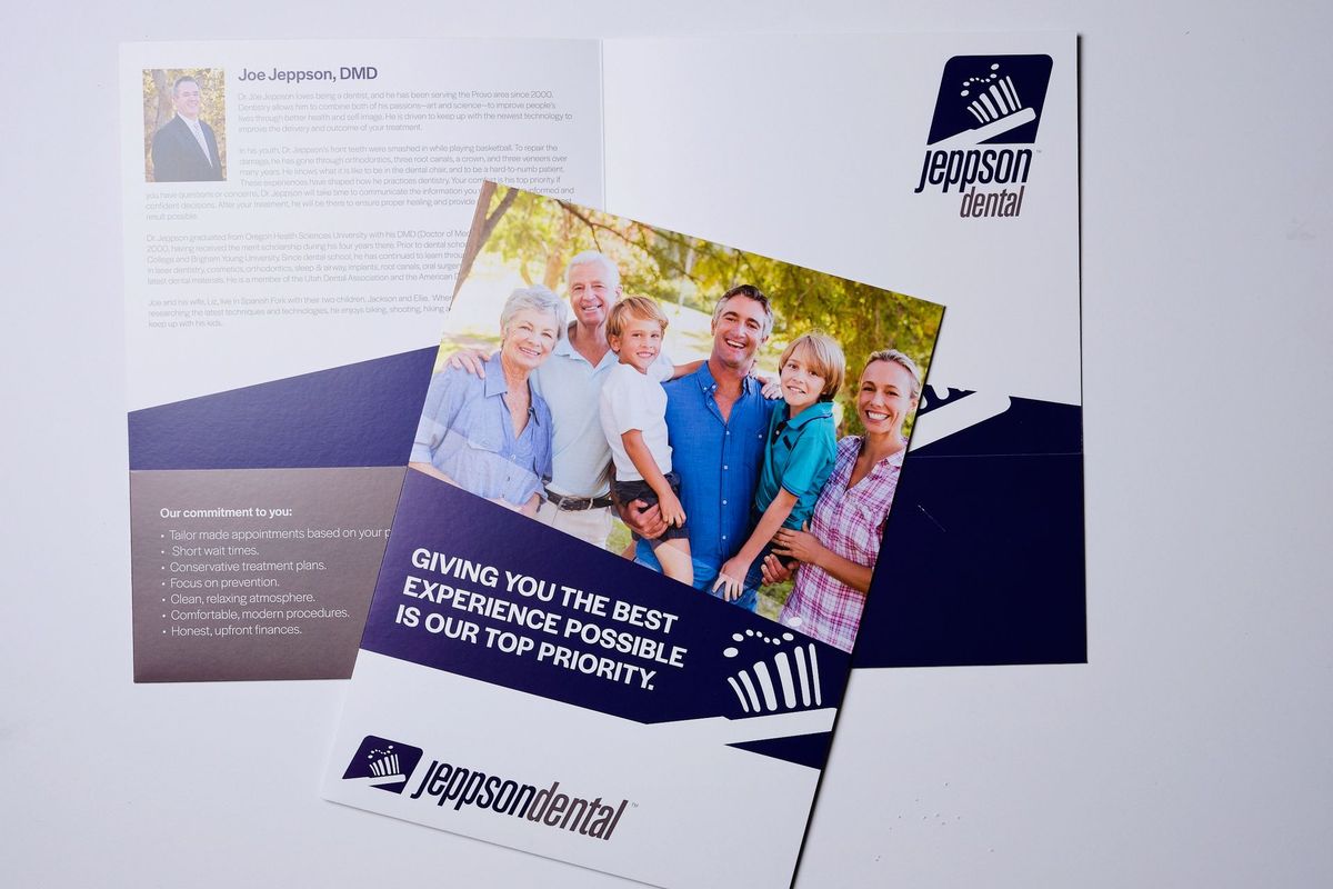 Open presentation folder for a dental practice, showing a printed bio page and navy pockets. A full-color insert with a smiling family photo lies on top.